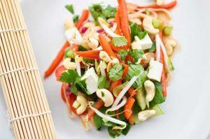 Plant-based tofu vegetable pad thai on white plate with lime