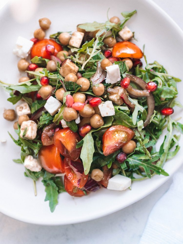 Chickpea, avocado, rocket, tomato, pomegranate, feta and mint salad with balsamic dressing on white plate